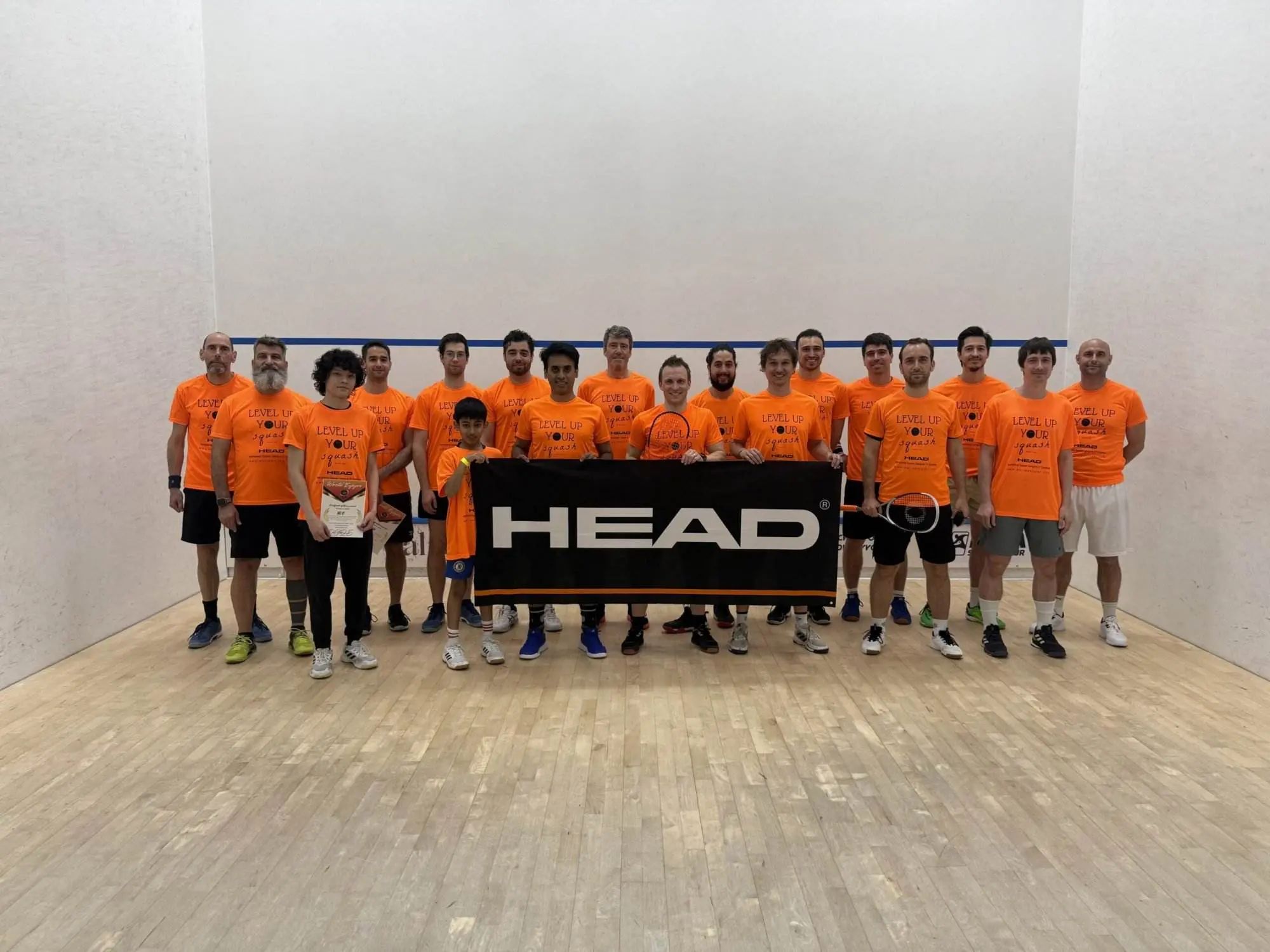 Participants d'un camp World Enjoyer en t-shirts orange, réunis sur un court de squash derrière une banderole HEAD