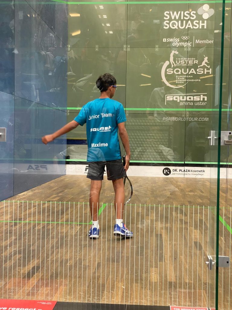 Maxime Rossier, de dos en tenue du Junior Team, sur le court vitré de la Squash Arena Uster