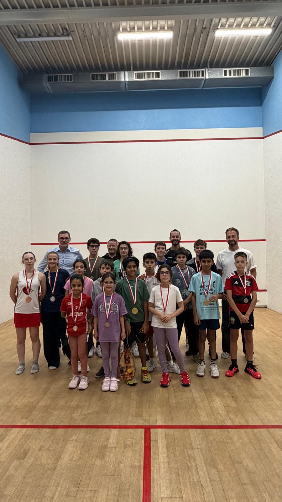 Les juniors des Championnats Romands 2026 posent sur un court, médaille au cou, entourés de quelques adultes